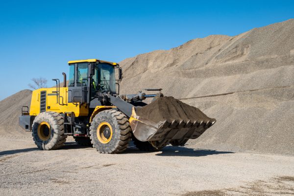 A large loader transports crushed rock or gravel in a bucket at a construction site or concrete plant. Concept of transporting bulk materials on construction equipment.